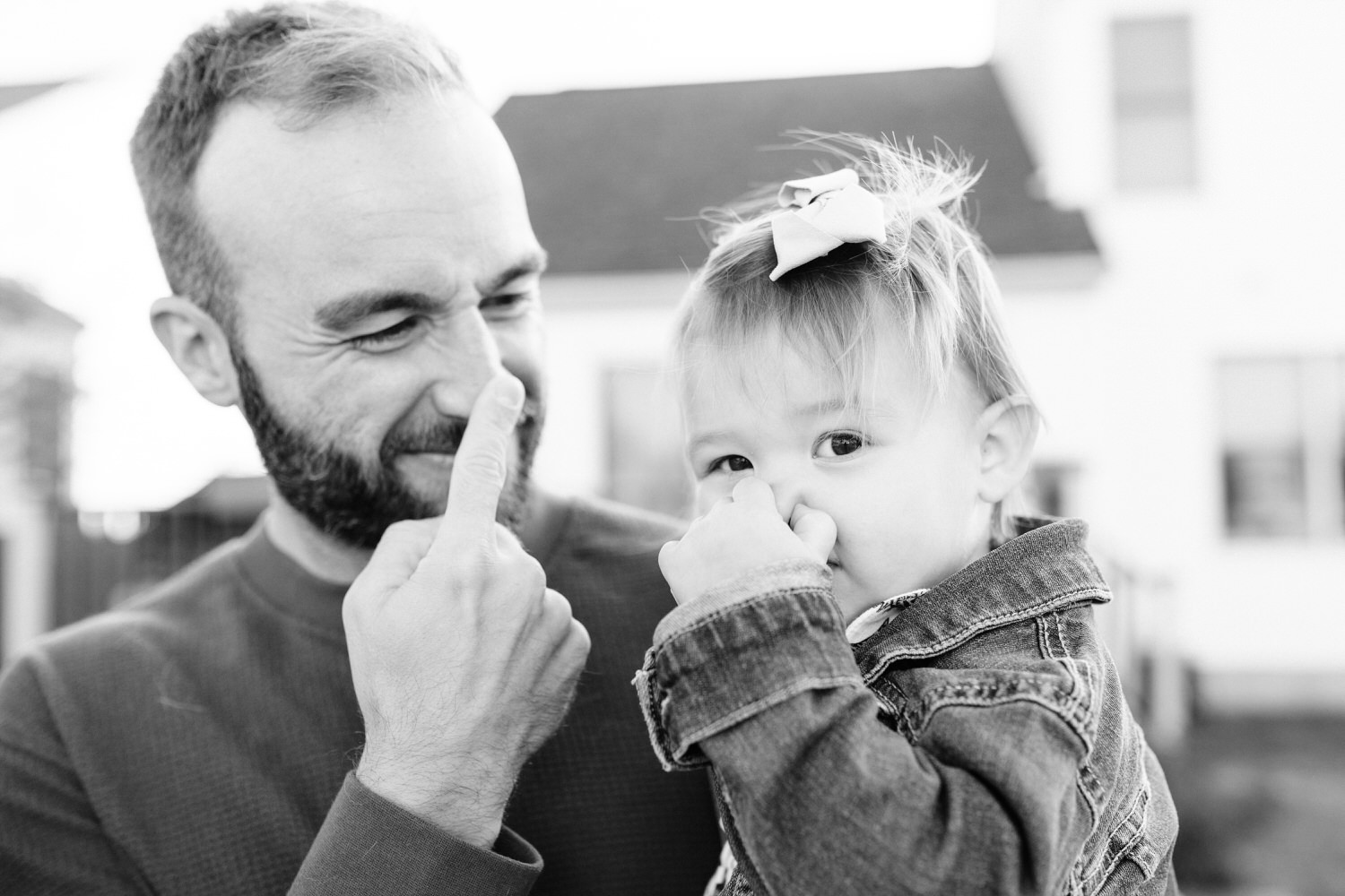 A father and his toddler daughter both touch their noses in a cute way