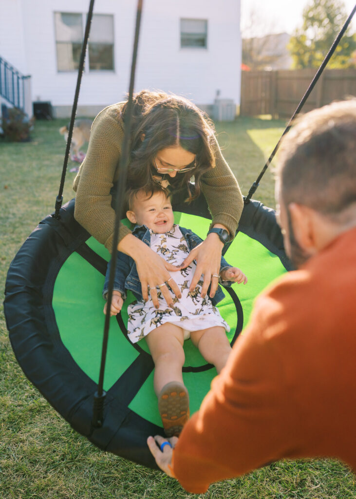 A toddler on a disc swing being pushed by her mom and dad