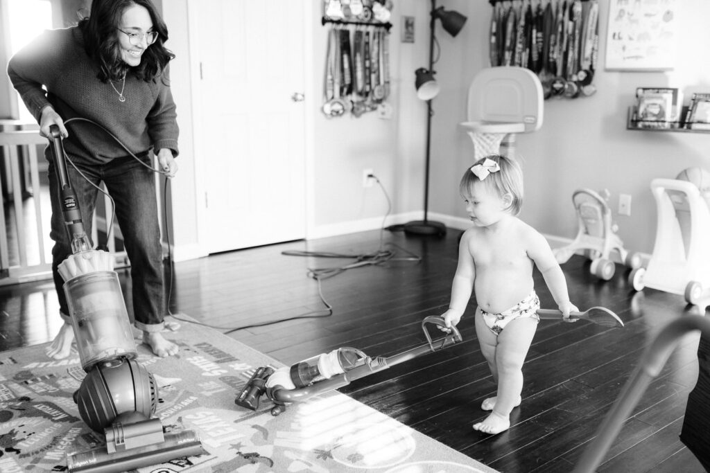 a mom vacuums with her toddler daughter who has a toy vacuum