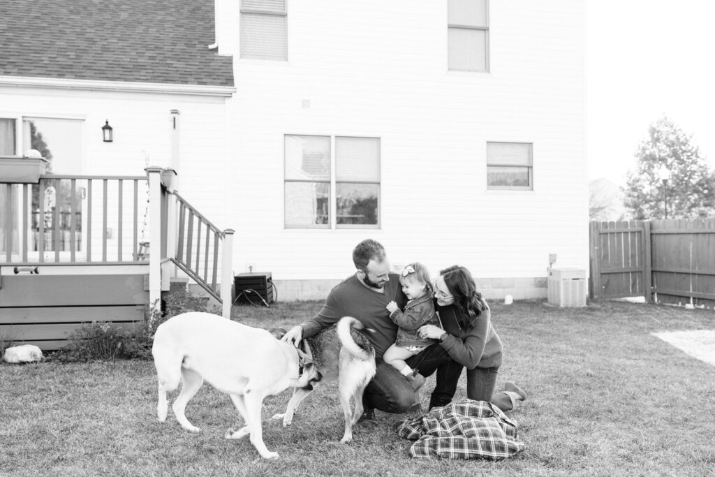 A family with a young toddler and two large dogs sitting on their lawn