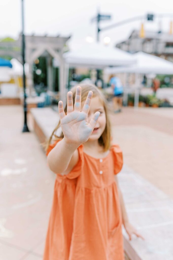 A little girl holds up her chalk covered hand in front of her face