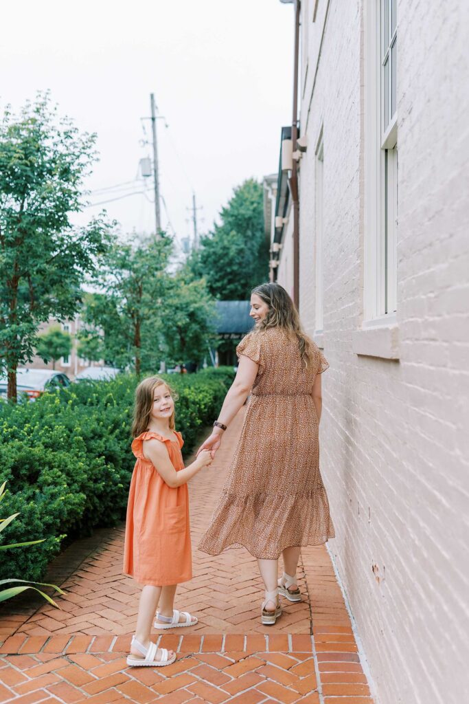 A little girl and her mom walking away down the sidewalk