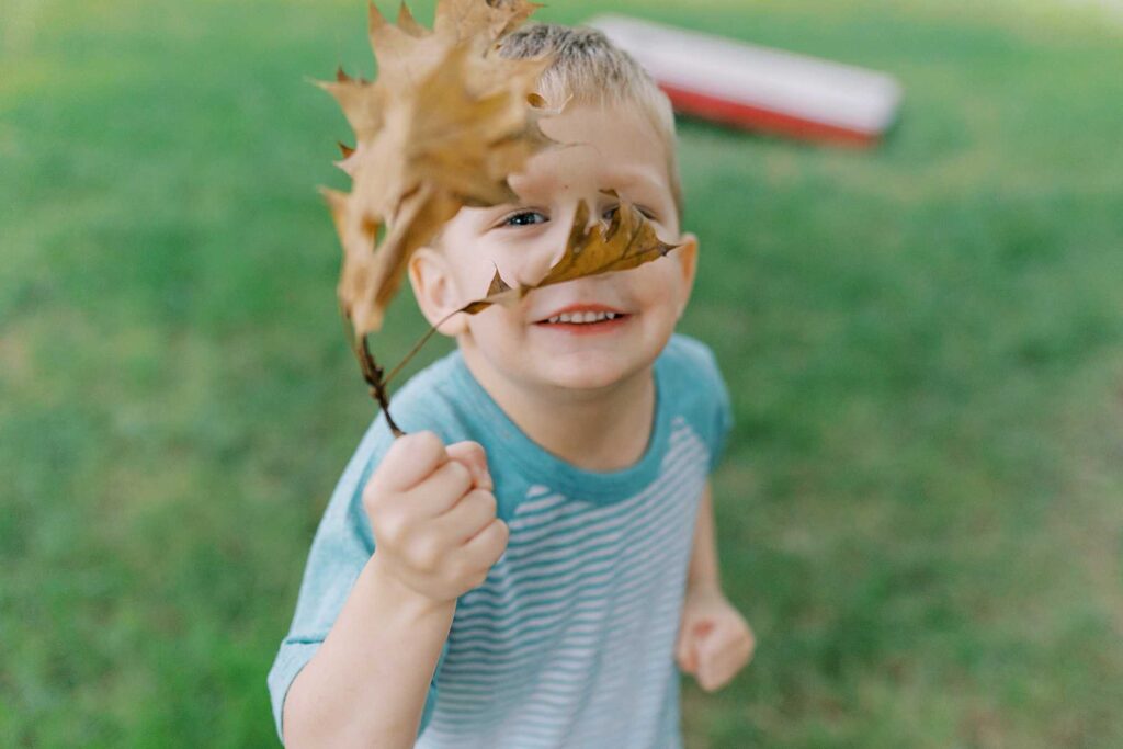A little boy holds a leaf in front of his face