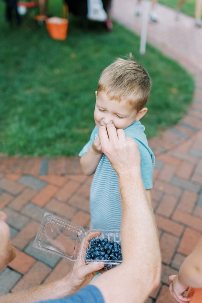 A dad's hand playfully shoves blueberries in his son's mouth