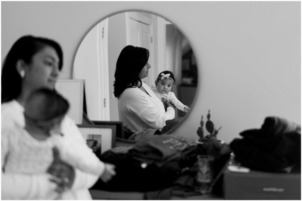 A mom holding her baby as the baby looks in a mirror at her reflection
