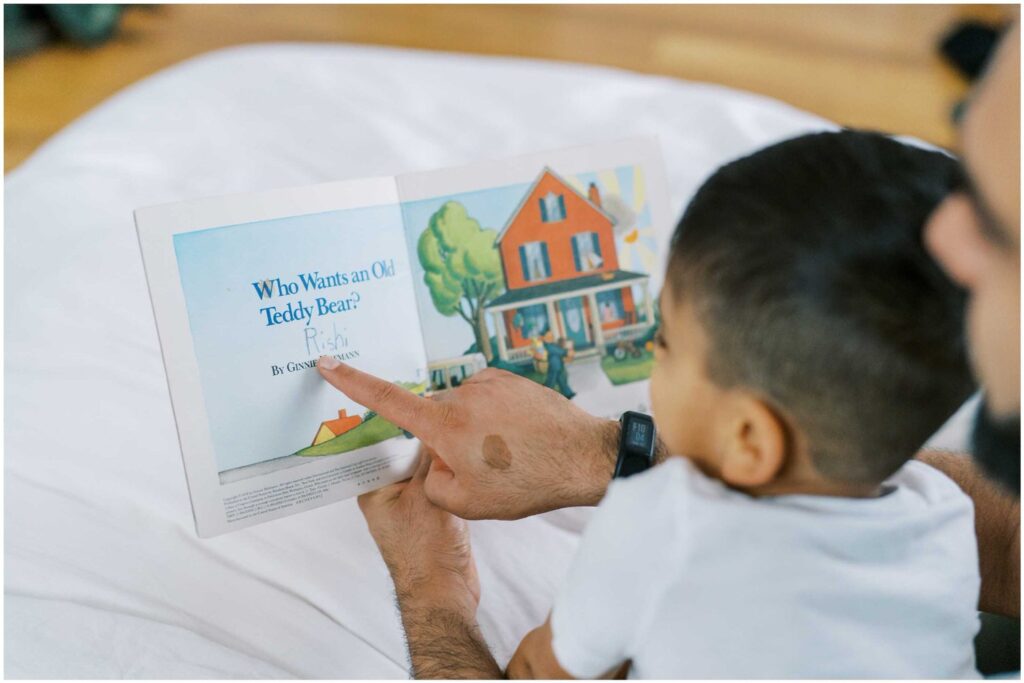 a close-up of a dad's finger pointing to pictures in a book as he reads to his son