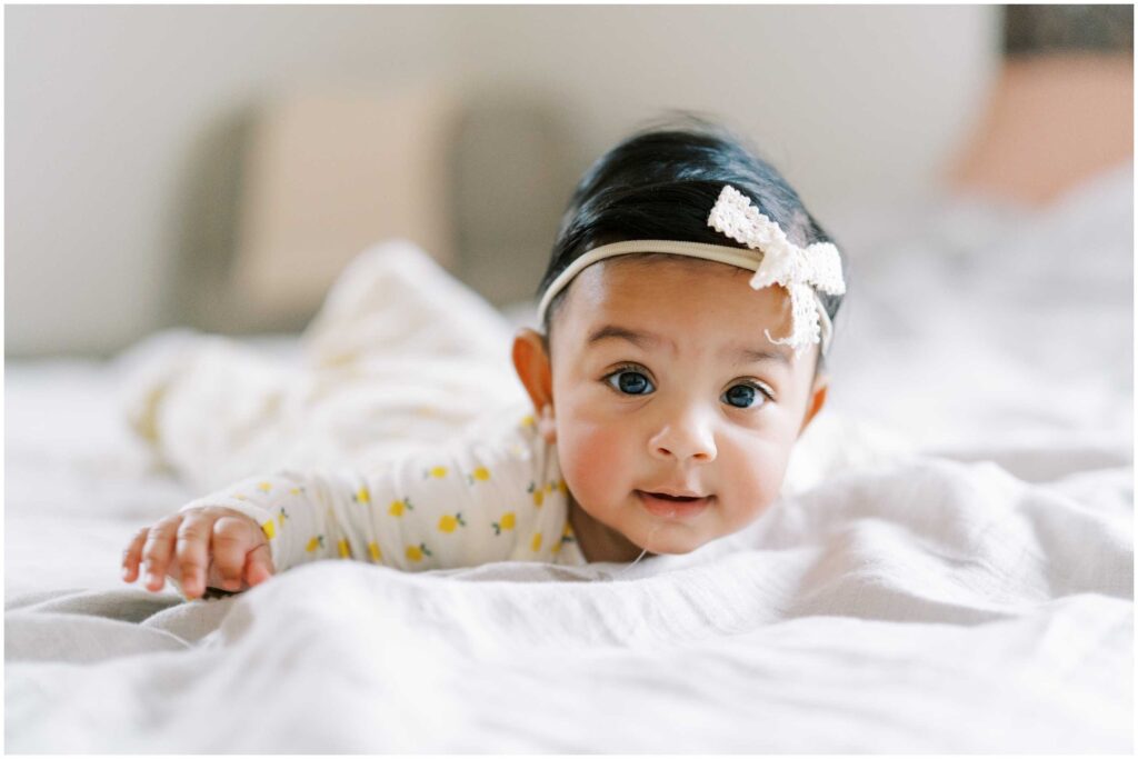 A baby girl wearing a bow headband doing the airplane pose in bed