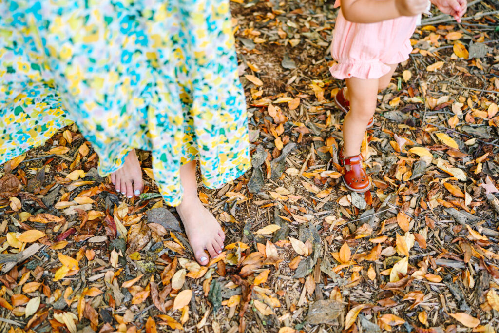 A close-up of a mom and daughter's feet walking through orange leaves