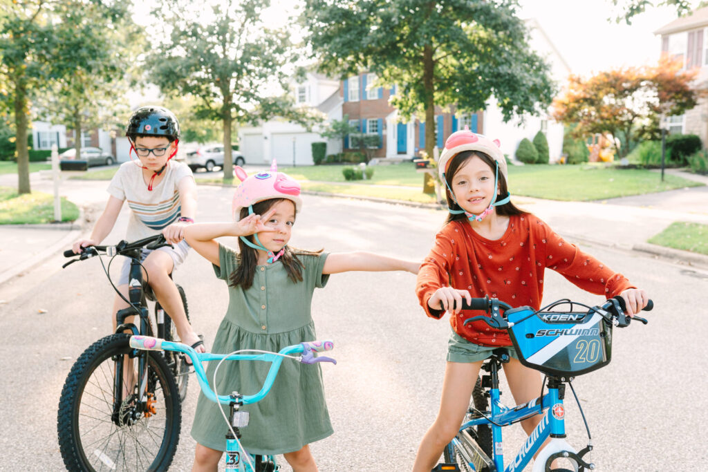 Three siblings wearing colorful helmets strike a silly pose on their bikes in their Columbus Ohio neighborhood