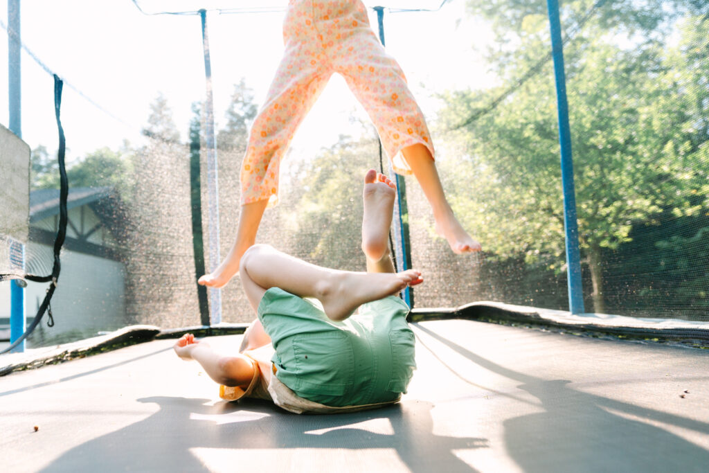 Siblings jump on a trampoline in their back yard in Columbus Ohio, captured by lifestyle photographer Daisy Zimmer
