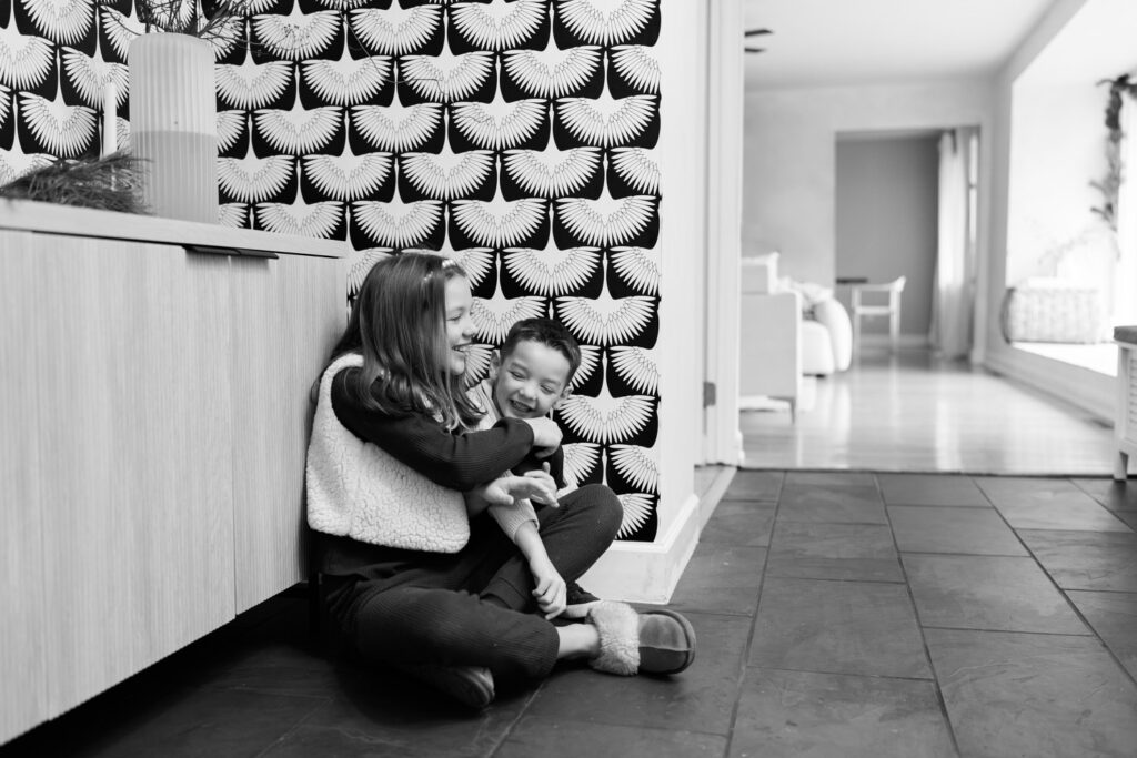 A brother and sister have a tickle fight in the foyer of their home in Columbus Ohio, captured by lifestyle photographer Daisy Zimmer