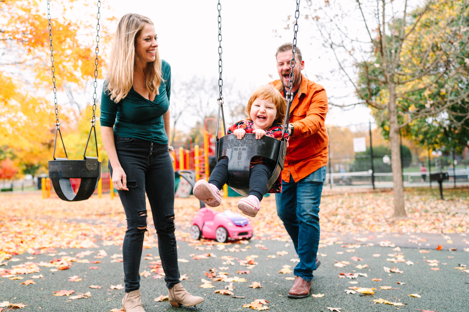 A mom and dad push their redhead daughter on a swing