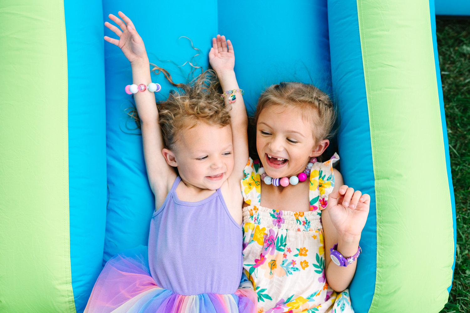 Two young sisters laughing together on an inflatable slide, captured by lifestyle photographer Daisy Zimmer