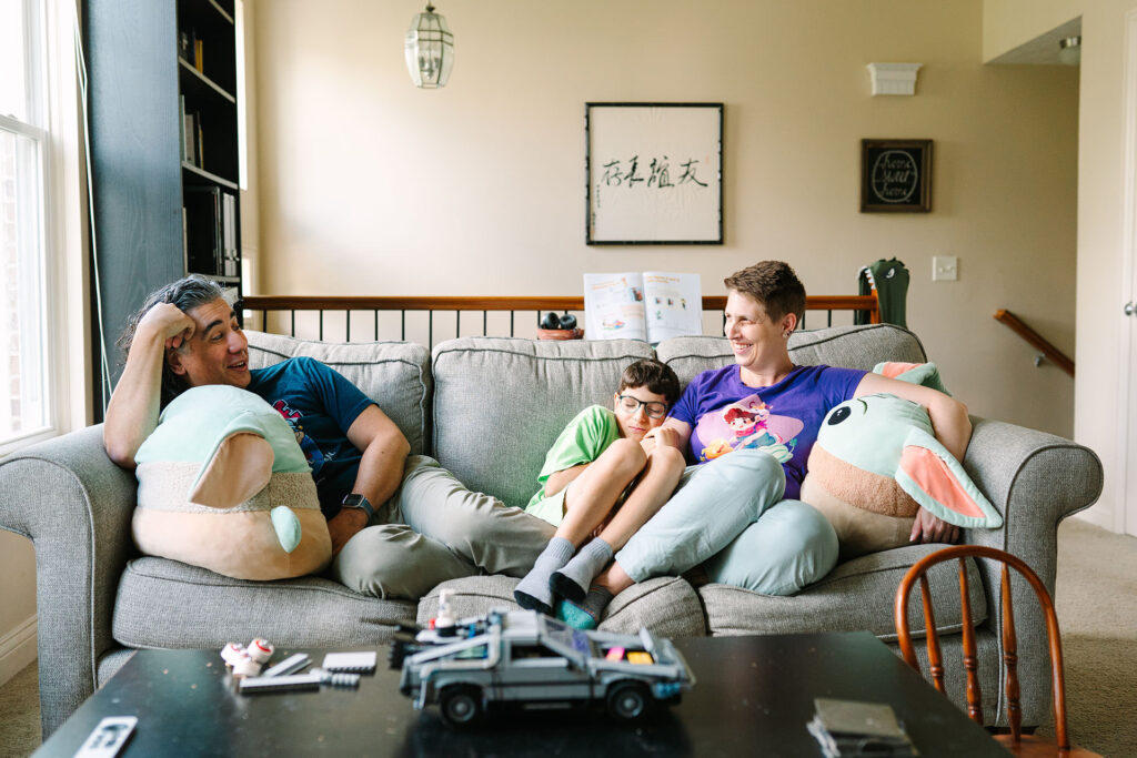 Chris and Rachelle sit with their son on the couch, a relaxed moment captured by lifestyle photographer Daisy Zimmer