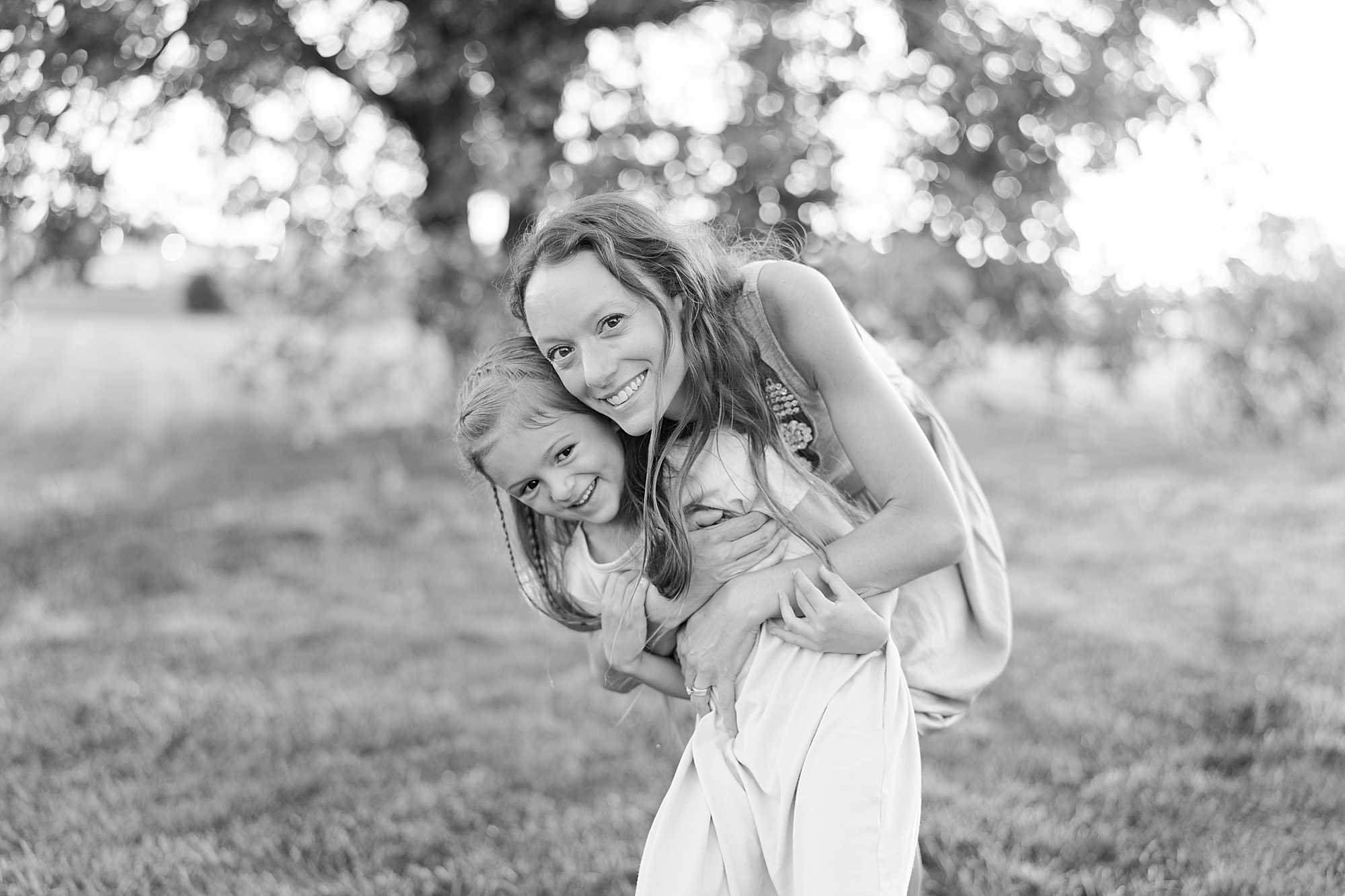 a mom hugs her daughter in front of a tree at sunset