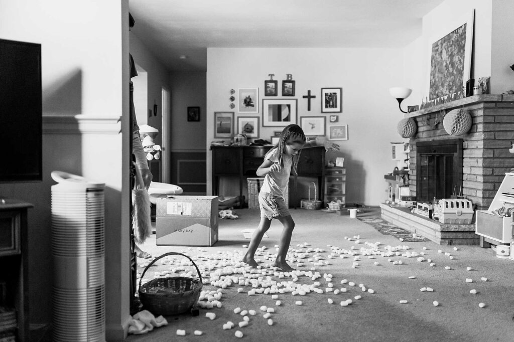 A young girl tiptoes over packing peanuts that spilled all over the living room floor