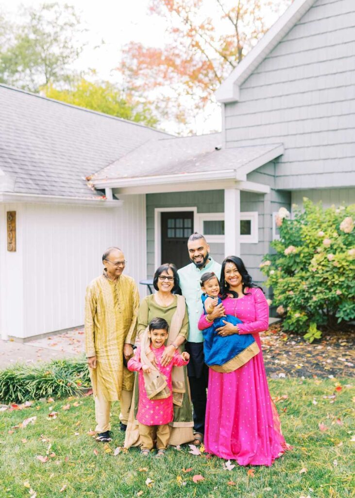 A family wearing traditional Indian attire standing in front of their house