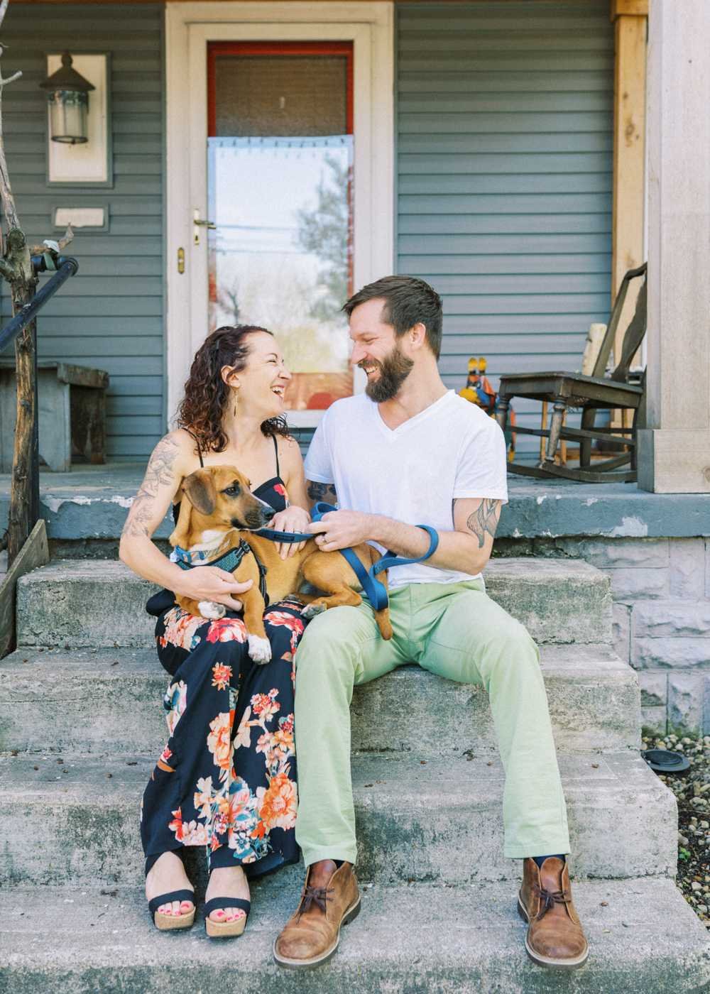 A husband and wife sit on the front steps of their house with their dog