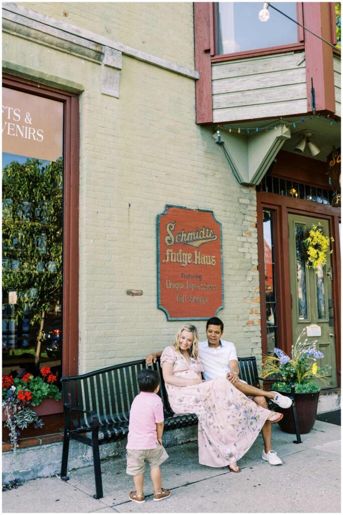 A family of three sitting on an iron bench in front of Schmidt's sausage house in German Village