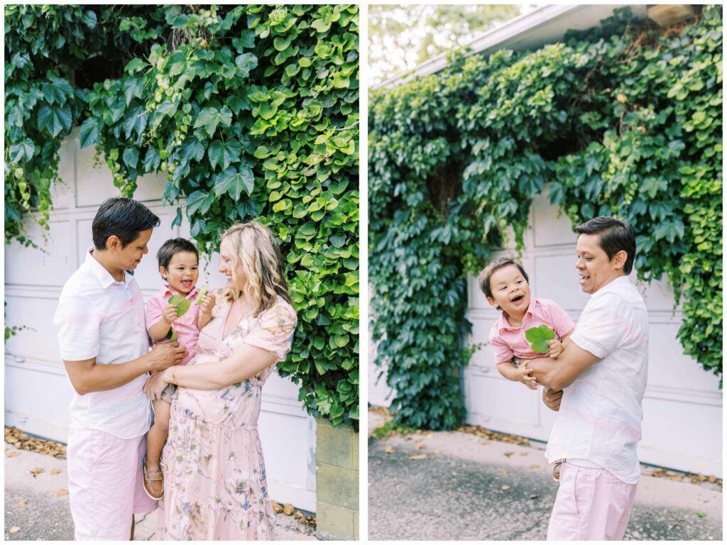 Mom and dad hold their toddler son in front of an ivy wall
