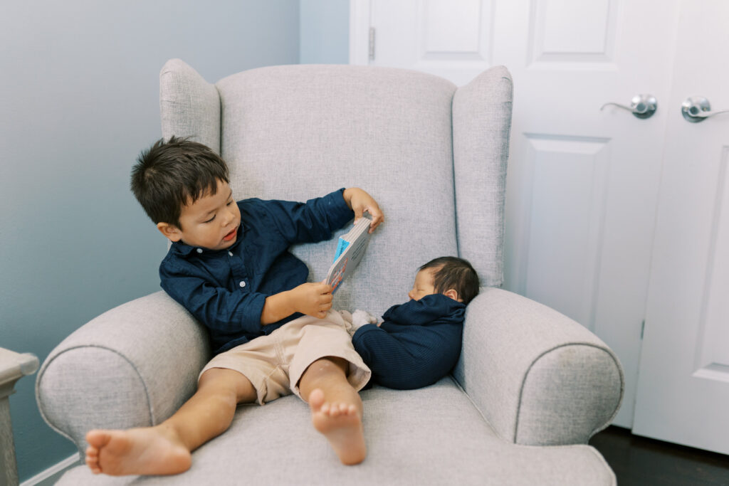 A toddler reads a book to his newborn sibling