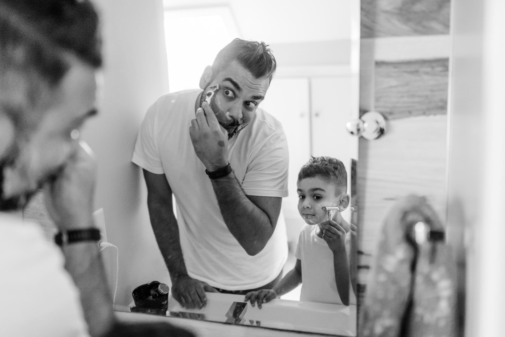 Dad and son shaving in the mirror together in their home