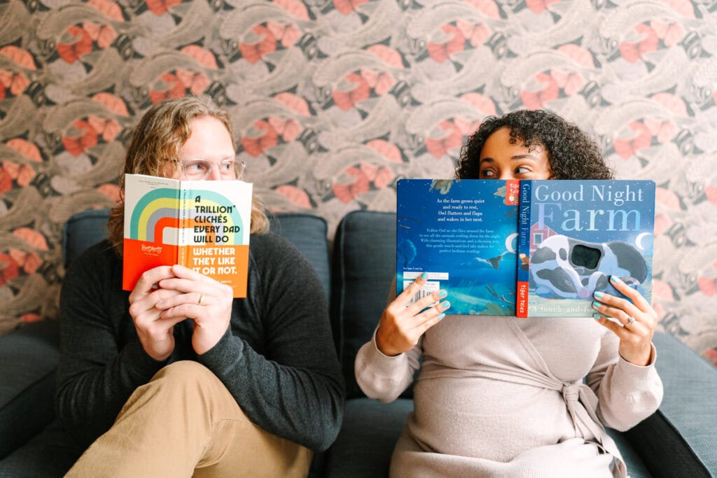 A candid portrait by Columbus newborn photographer, Daisy Zimmer, of a husband and wife reading baby books and glancing at each other lovingly 