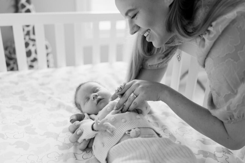 A black and white portrait by Columbus Ohio newborn photographer, Daisy Zimmer, of a mom smiling down at her baby in a crib