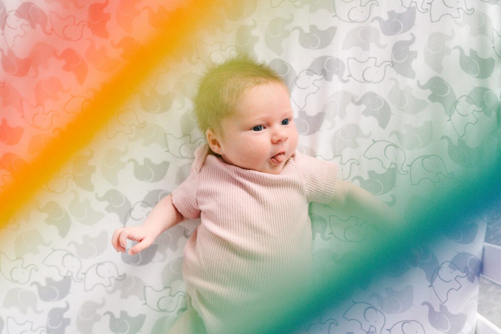 Newborn baby Jovie in her crib surrounded by rainbow colors