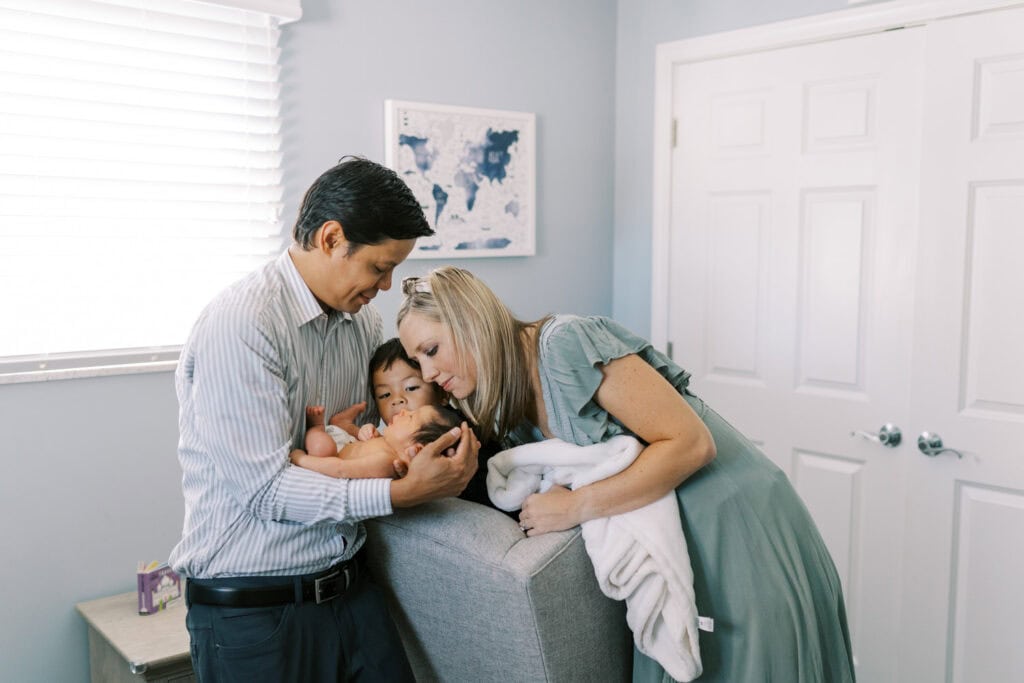 A family with a toddler gathers around the newborn baby and looks at her closely