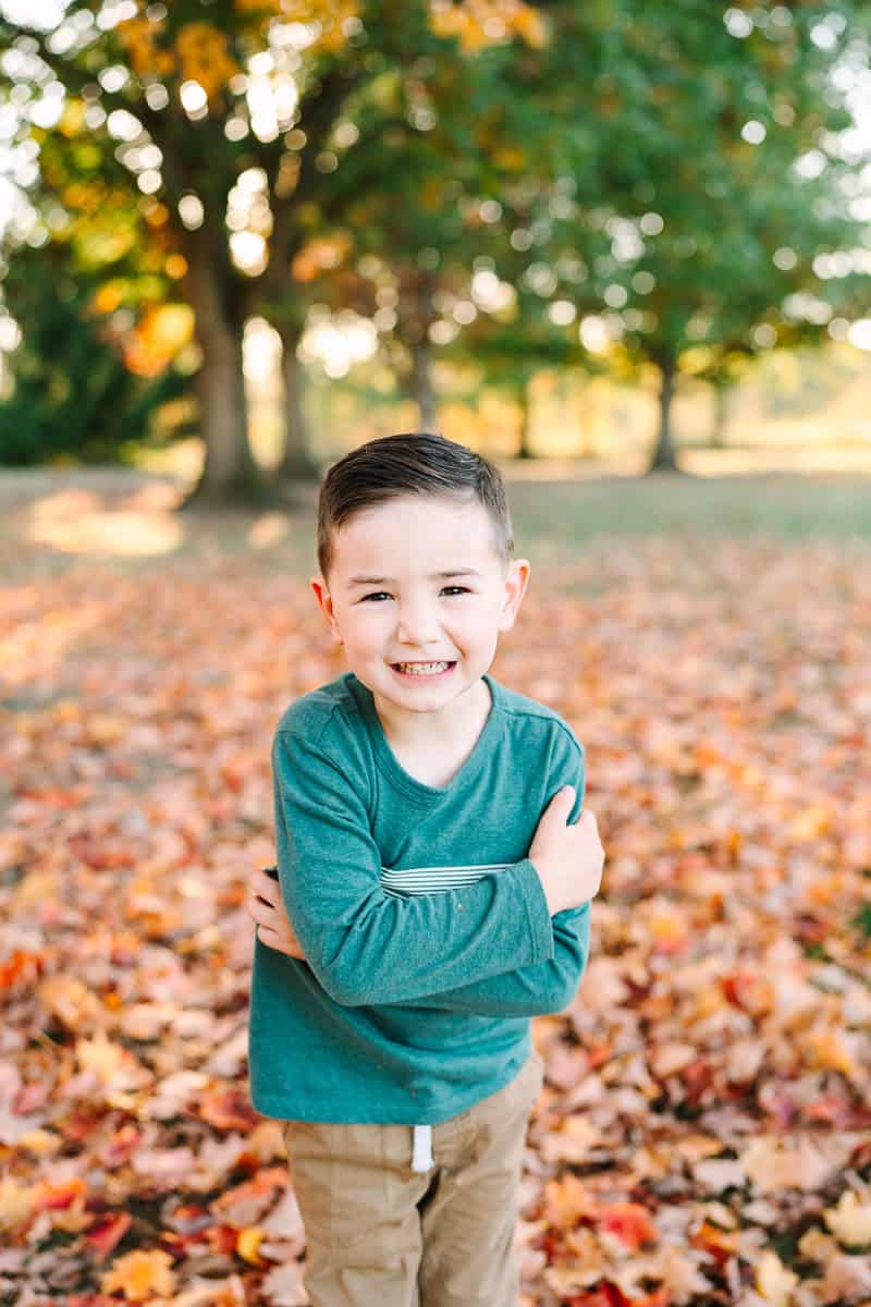 A young boy crossing his arms in front of his chest and smiling, captured during a fall mini session by Daisy Zimmer Photography