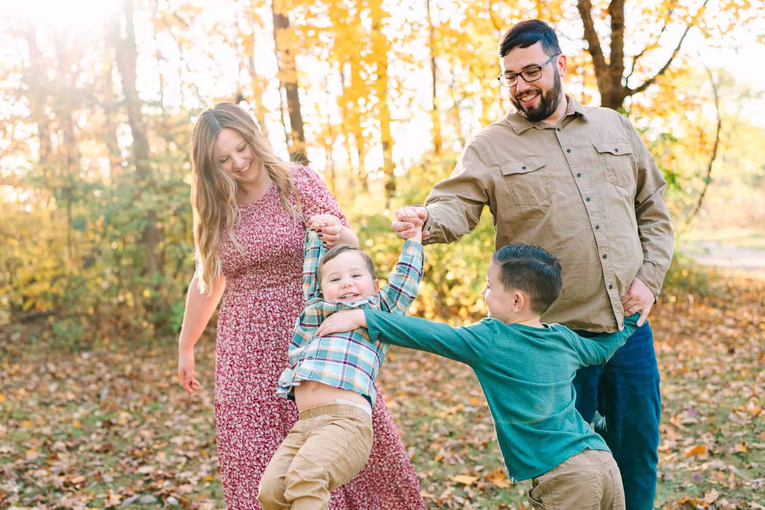 A family plays together in a park in front of autumn trees, captured during a fall mini session by Daisy Zimmer Photography