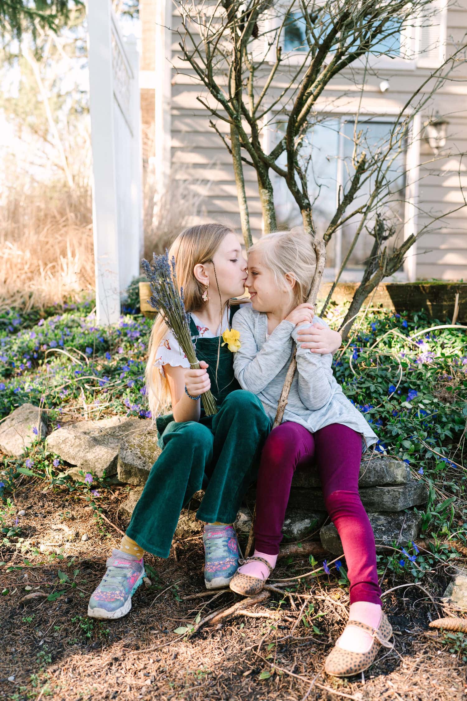 Young sisters holding flowers share a sweet embrace in the Springtime.